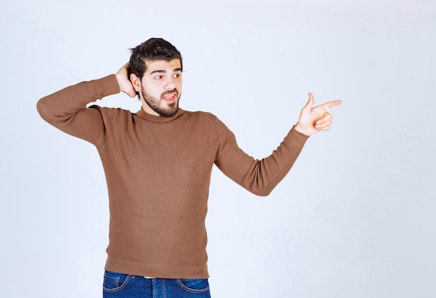 Image of a young smiling man model standing and pointing away with an index finger. High quality photo