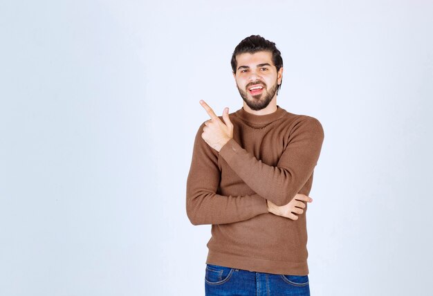 Image of a young smiling man model standing and pointing up with an index finger . High quality photo