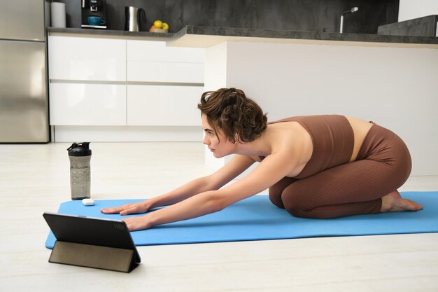 Foto gratuita immagine di una giovane sportiva che fa yoga a casa e guarda un video tutorial di un istruttore di ginnastica su un tablet stretch