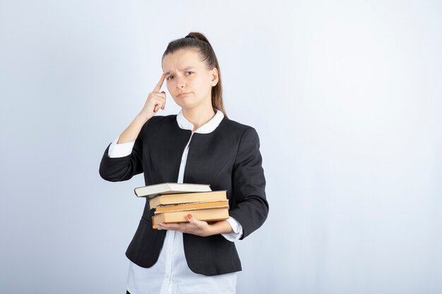 Image of young student with bunch of books thinking on white.