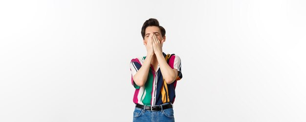 Image of young stylish man sneezing in hands standing over white background