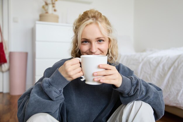 Image of young teenage girl sitting in her bedroom on floor drinking cup of tea and enjoying day at