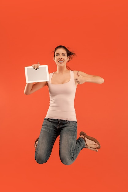 Image of young woman over blue space using laptop computer or tablet gadget while jumping