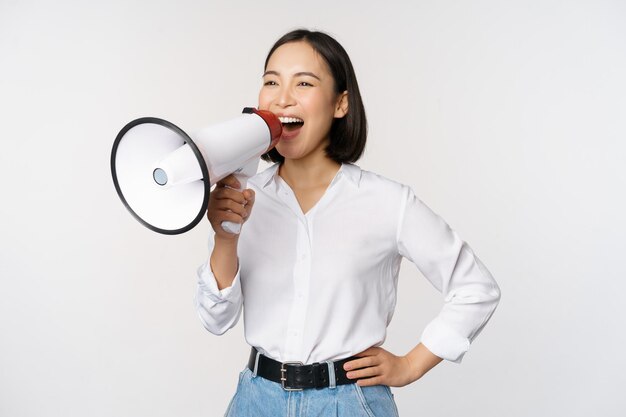 Image of young woman korean activist recruiter screaming in megaphone searching shouting at loudspeaker standing over white background