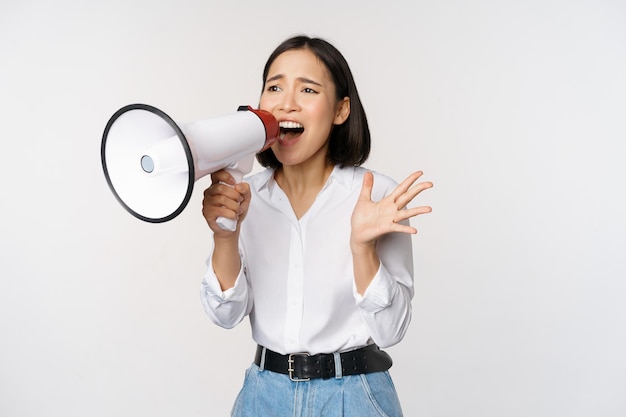 Image of young woman korean activist recruiter screaming in megaphone searching shouting at loudspeaker standing over white background