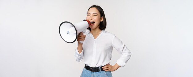 Free photo image of young woman korean activist recruiter screaming in megaphone searching shouting at loudspeaker standing over white background