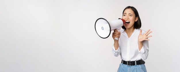 Image of young woman korean activist recruiter screaming in megaphone searching shouting at loudspeaker standing over white background