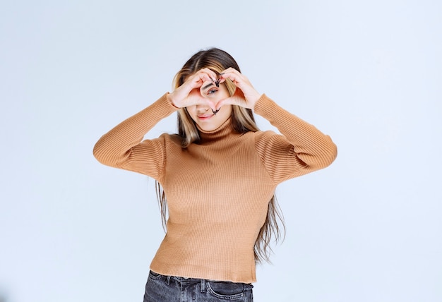Image of a young woman model in brown sweater doing heart symbol shape with hands.