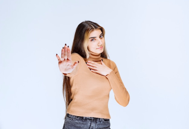 Изображение модели молодой женщины в коричневом свитере стоя и делая знак остановки.