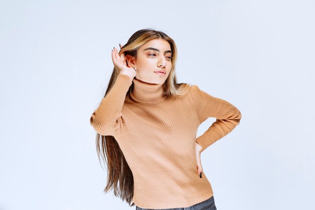 서서 포즈를 취하는 갈색 스웨터를 입은 젊은 여성 모델의 이미지.