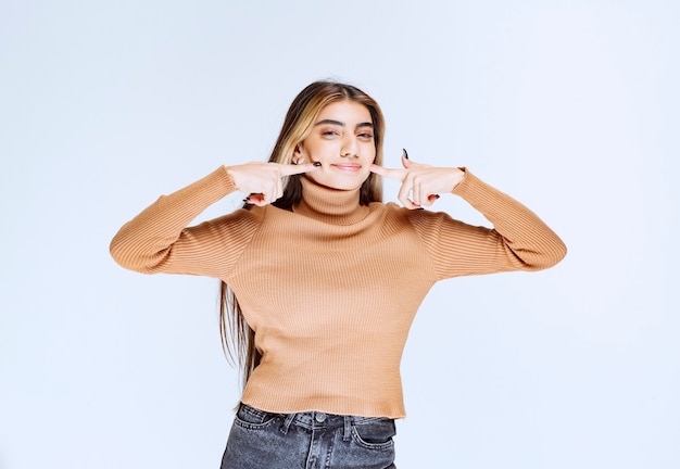 Immagine di un modello di giovane donna in maglione marrone in piedi e toccando le guance.