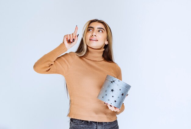 선물 상자가 가리키는 갈색 스웨터를 입은 젊은 여성 모델의 이미지.