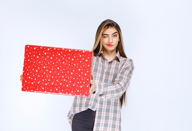 Free photo image of a young woman model standing and holding a red gift box.