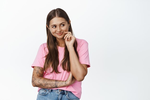 Image of young woman smiling and thinking, looking aside intrigued, has interesting idea, ponder something, white background.