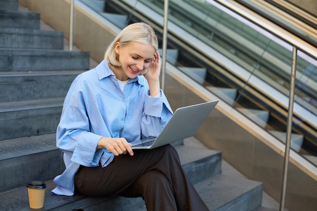 Free photo image of young woman student studying online working remotely sitting on stairs with laptop and