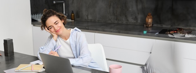 Free photo image of young woman works on laptop at home productive girl studies in her kitchen on computer