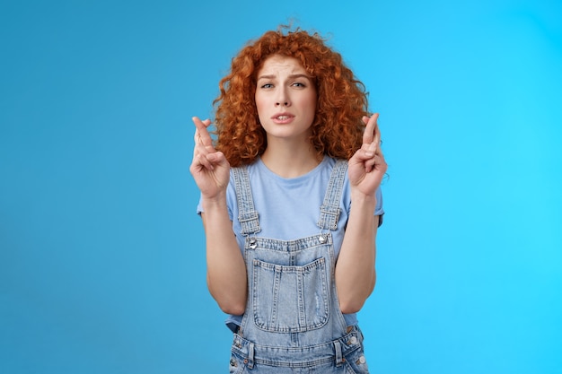 Free photo impatient worried hopeful pretty ginger girl curly hairstyle squinting intense stare praying cross fingers good luck awaiting important news willing wish come true achieve desire dream fulfill.