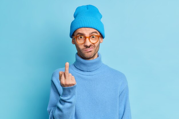 Impolite handsome man shows fuck off sign being rude and looks dissatisfied at camera