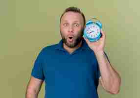 Free photo impressed adult slavic man holding alarm clock looking