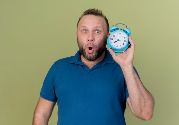 Impressed adult slavic man holding alarm clock looking 