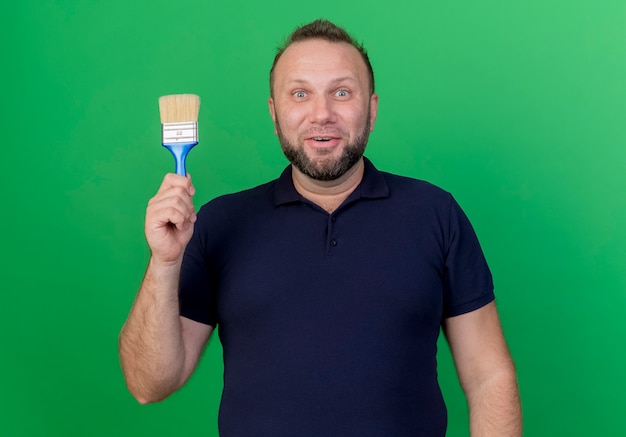 Impressed adult slavic man looking holding paint brush isolated