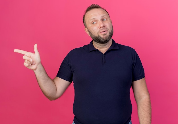 Impressed adult slavic man looking at side and pointing at side isolated on pink wall