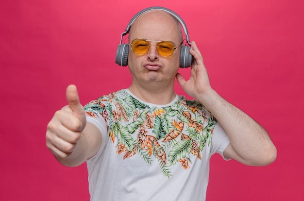 Бесплатное фото Впечатленный взрослый славянский мужчина в темных очках и в наушниках, листая пальцем вверх