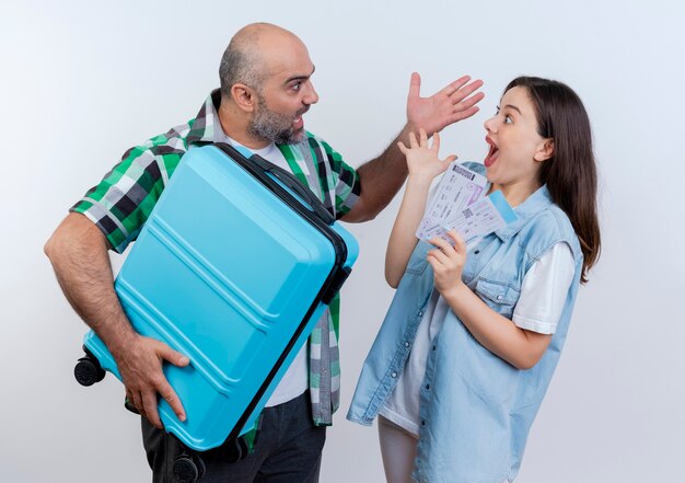 Impressed adult traveler couple man holding suitcase woman holding travel tickets both keeping hand in air and looking at each other