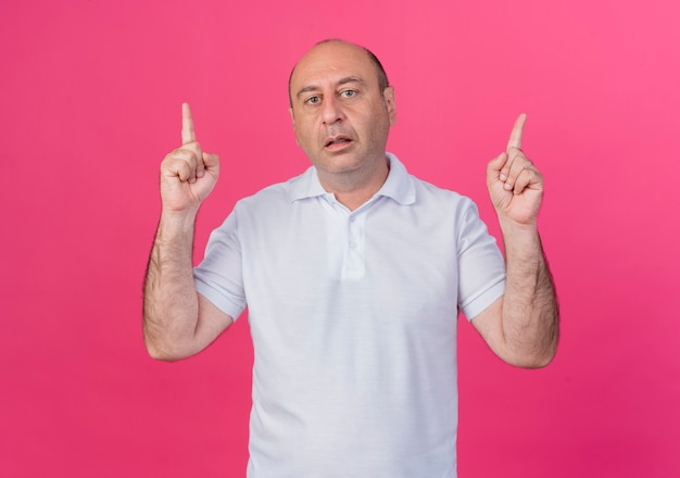 Impressed casual mature businessman pointing up  isolated on pink background