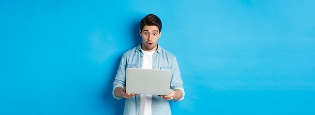 Впечатленный кавказский парень с удивлением смотрит на экран ноутбука, проверяя промо в интернет-киоске