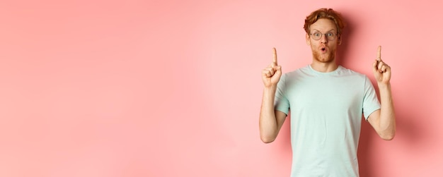 Impressed caucasian man with ginger hair wearing glasses and tshirt saying wow and pointing fingers