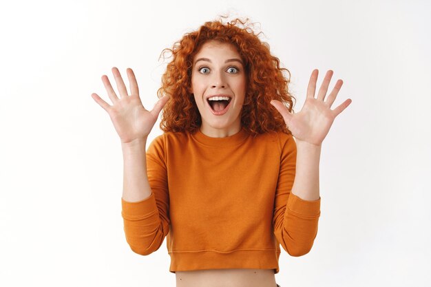 Impressed cheerful attractive redhead woman, curly hairstyle raising hands up, telling incredible awesome news, smiling broadly shaking arms joyfully react surprised and thrilled good event