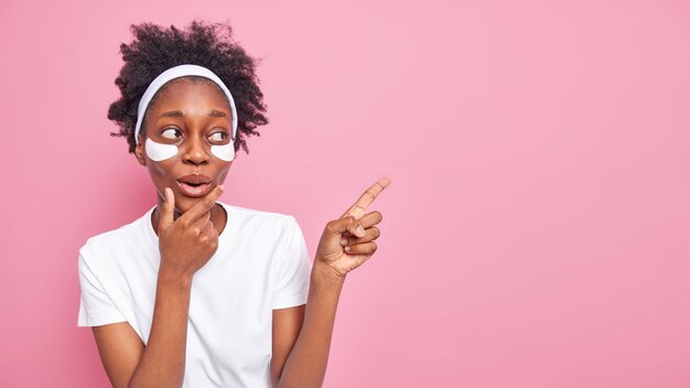 Impressed dark skinned woman holds chin has thin face 