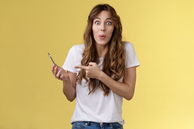 Impressed enthusiastic good-looking girl amused  stares at camera  holding smartphone