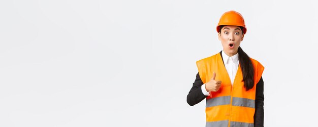 Impressed and excited asian female engineer in safety helmet and reflective jacket fascinated with n