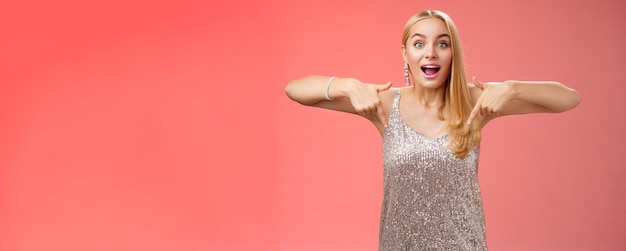 Free photo impressed excited attractive glamour blond girl in silver glittering dress gasping thrilled pointing