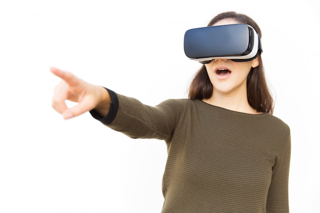 Impressed excited woman in VR headset pointing finger away