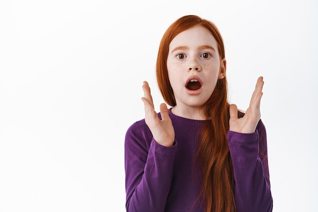 Free photo impressed ginger girl with freckles gasping, clap hands and look amazed and astounded with impressive awesome thing, checking out, standing over white background