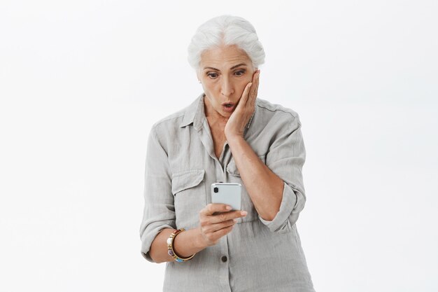 Impressed grandmother looking at smartphone screen amazed