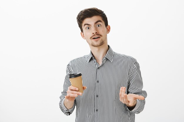 Impressed guy sharing thoughts with friend after attending great meeting. Curious good-looking male model with moustache and beard, pointing during conversation, drinking coffee in cafe