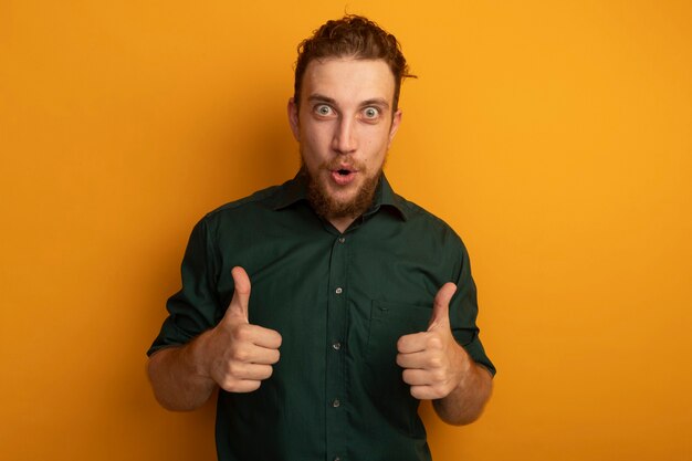Impressed handsome blonde man thumbs up of two hands isolated on orange wall
