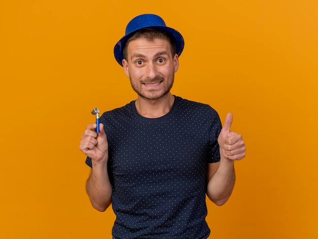 Впечатленный красавец в синей партийной шляпе показывает палец вверх и держит партийный свисток на оранжевой стене с копией пространства