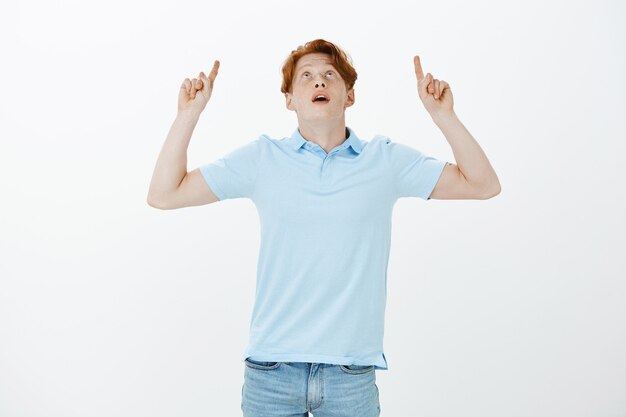 Impressed handsome redhead man pointing fingers up