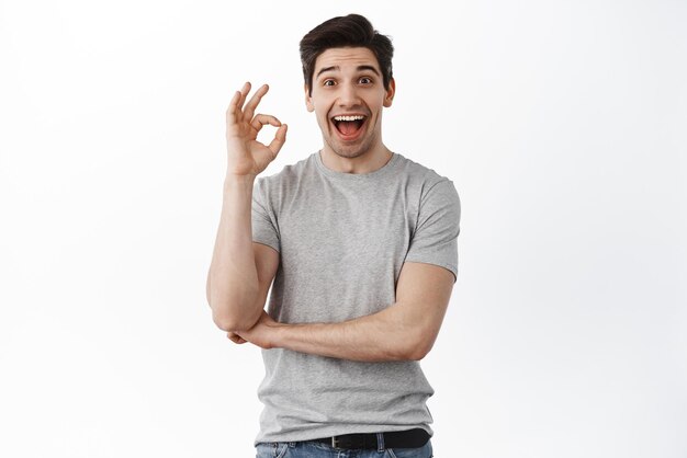 Impressed happy man say yes show okay sign and nod in approval satisfied with good result praise excellent thing standing against white background