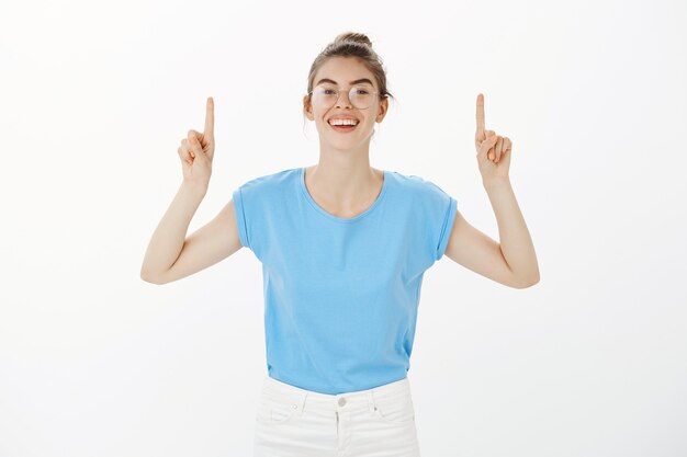 Impressed happy woman pointing fingers up, showing advertisement with joyful smile