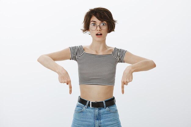 Impressed hipster girl in cropped top pointing fingers down