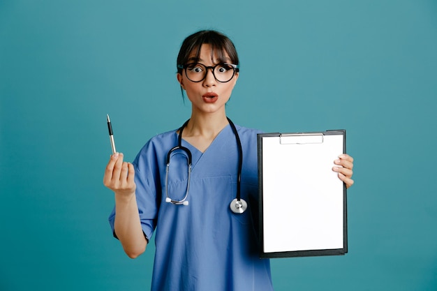 Free photo impressed holding clipboard young female doctor wearing uniform fith stethoscope isolated on blue background