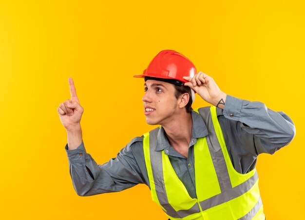 Impressed looking up young builder man in uniform points at up 