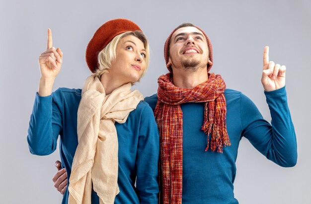 Impressionato la ricerca di una giovane coppia il giorno di san valentino che indossa un cappello con una sciarpa punta in alto isolato su sfondo bianco