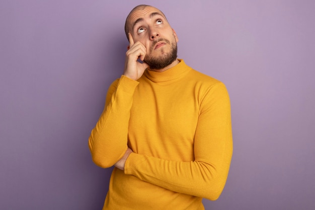 Free photo impressed looking up young handsome guy putting hand on cheek isolated on purple wall